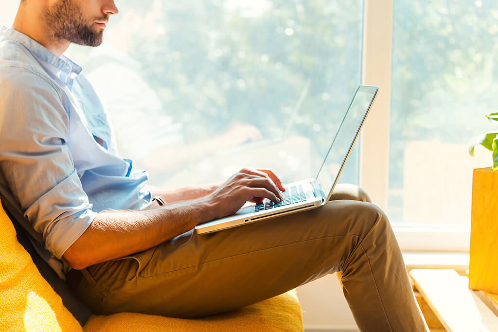 Close-up of young man working on laptop while sitting in a home, concept of executive alcohol and drug rehab