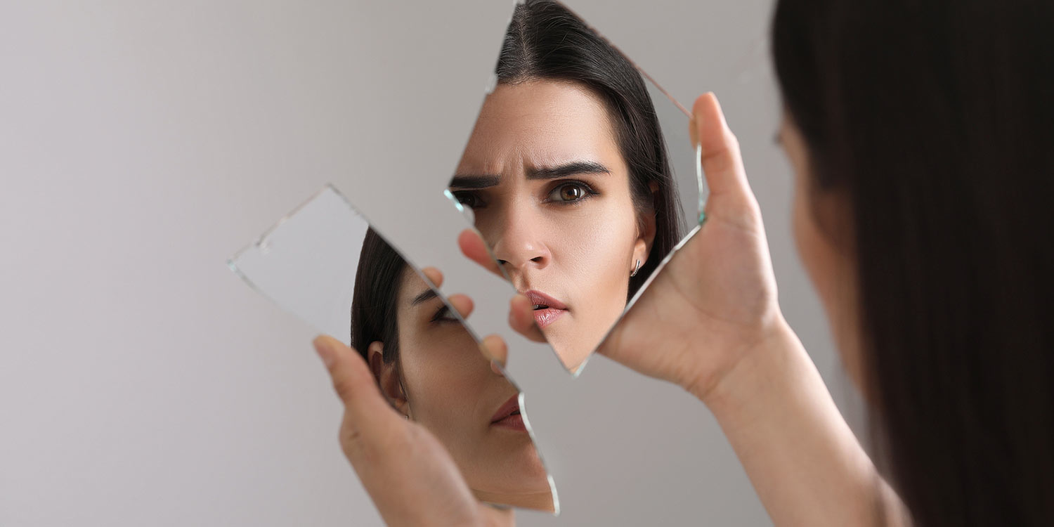 Opiates and Personality Concept: Young woman looking at herself in shard of broken mirror on light grey background, closeup